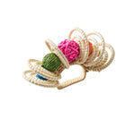 The Kim Seybert Calypso Napkin Ring features circular woven straw rings reminiscent of raffia and colorful balls in green, pink, orange, and blue, shown against a white background.
