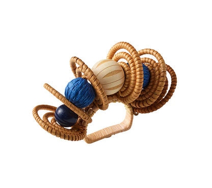 The Calypso Napkin Ring by Kim Seybert features woven rattan circular loops and hand-dyed wooden beads in blue, cream, and dark blue—perfect for beach table decor or adding a playful touch to your setting.
