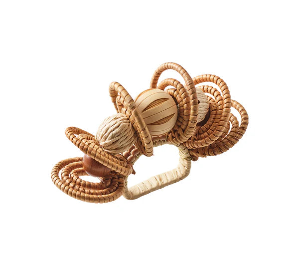 The Calypso Napkin Ring by Kim Seybert features woven rattan loops, raffia-wrapped bands, and a central sphere, displayed on a white background.