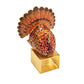 A Kim Seybert Turkey Trot Napkin Ring featuring a gold-toned square base topped with a metallic, multi-colored turkey figurine for Thanksgiving table decor.