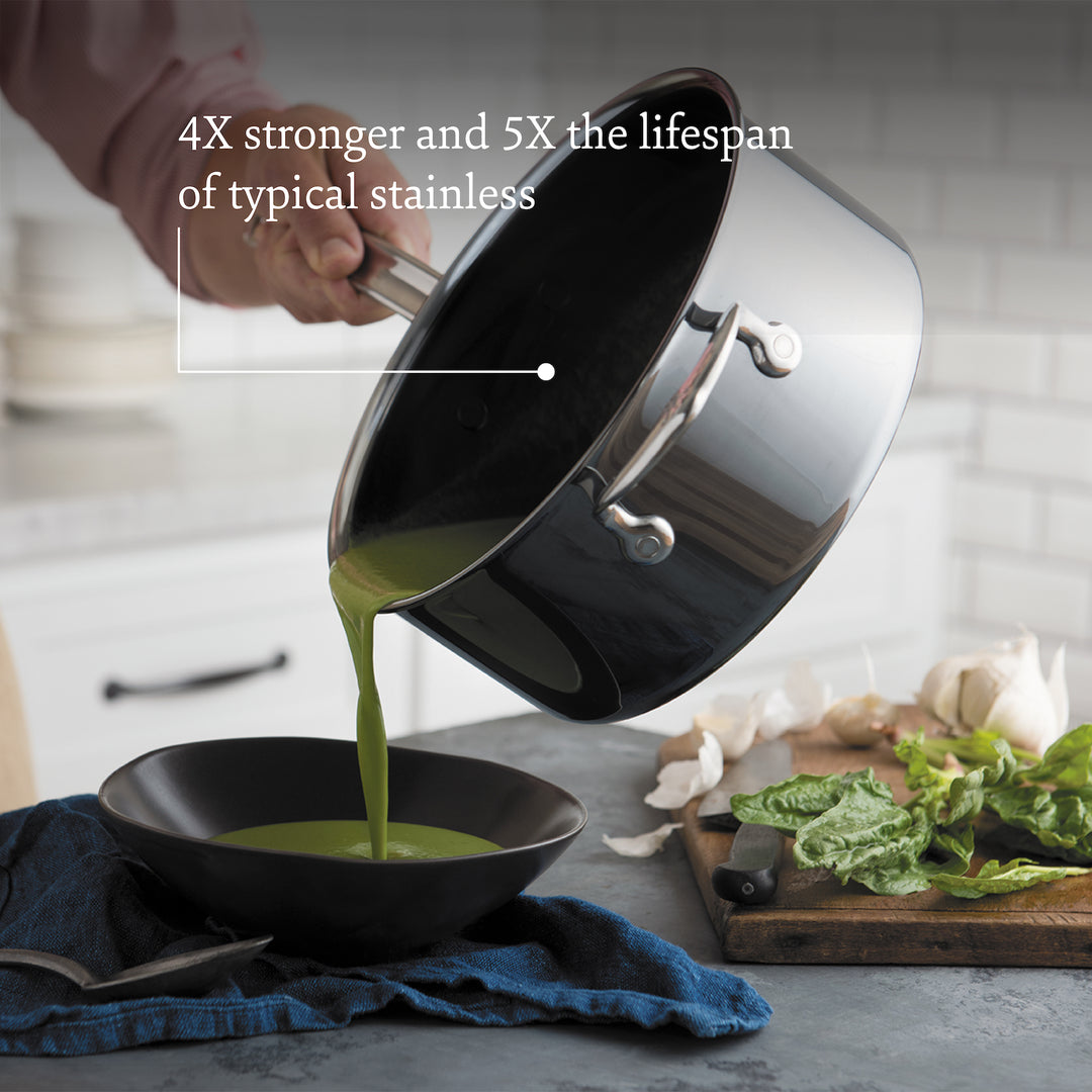 A person pours green soup from a Hestan NanoBond Titanium Ultimate Cookware pot into a black bowl beside a cutting board with greens and garlic. Text overlay highlights the set’s durability, ProCore aluminum core, and long-lasting performance.