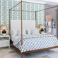 A bedroom featuring the Julian Chichester Rita Cane Wrap Four Poster Bed, white and patterned bedding, two bedside tables each with a lamp, and green leafy wallpaper behind the bed.