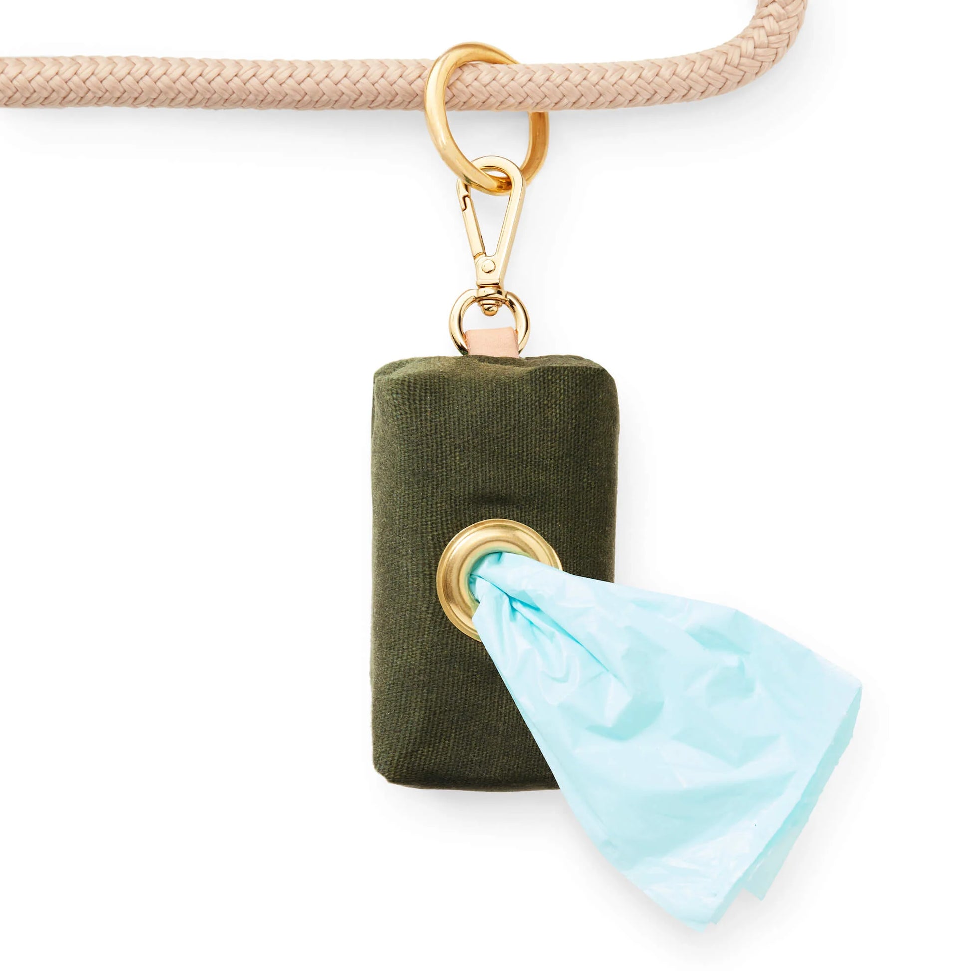 The Foggy Dog’s Waste Bag Dispenser in Olive is a stylish green fabric accessory, featuring a gold clip on a beige rope and dispensing light blue pet waste bags neatly through a metal grommet.
