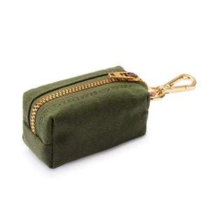 The Waste Bag Dispenser in Olive by The Foggy Dog is a small green fabric pouch featuring a gold zipper and a matching gold clip at one end, displayed against a white background. This chic dog accessory discreetly holds your waste bags and keeps them stylishly at hand during every walk.