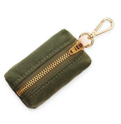 The Foggy Dog Waste Bag Dispenser in Olive is a small rectangular fabric pouch in olive green, featuring a gold zipper and coordinating gold key clip—designed as an elegant dog accessory that serves perfectly as a chic and stylish poop bag holder.