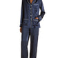 A person models Olivia von Halle’s Coco Silk Pajamas in navy with white piping—featuring a long-sleeve button-up top and matching pants—standing barefoot against a white background.