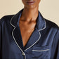 Close-up of a person wearing the Olivia von Halle Coco Silk Pajama top in navy with white piping and a chest pocket, set against a plain beige background.