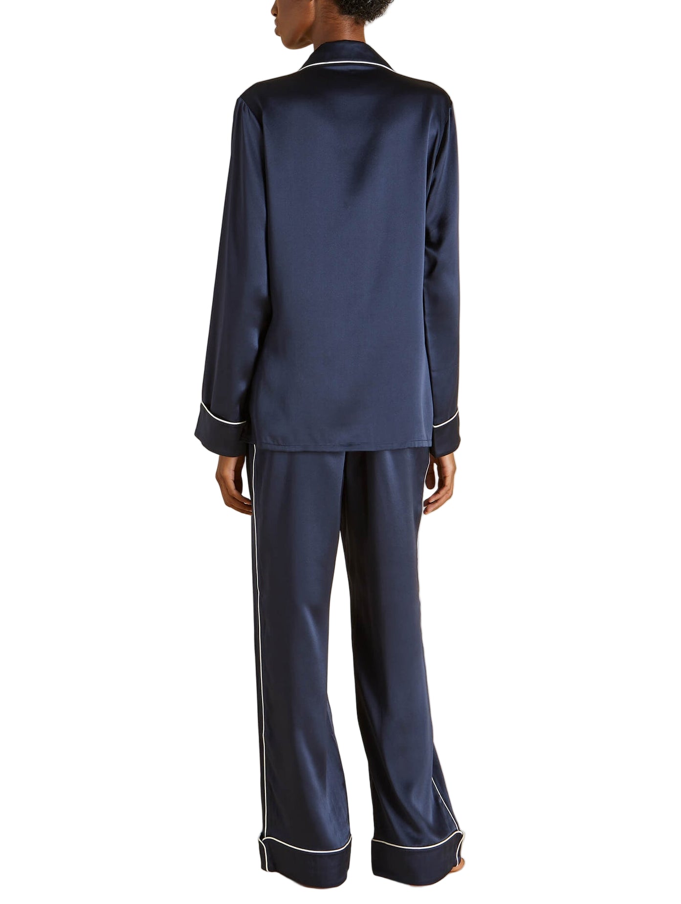 Someone is seen from the back wearing the Olivia von Halle Coco Silk Pajamas, a matching navy set with white piping.