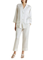 Wearing Olivia von Halle’s Fifi Silk Pajamas with flat sandals, channeling effortless style against a plain background.