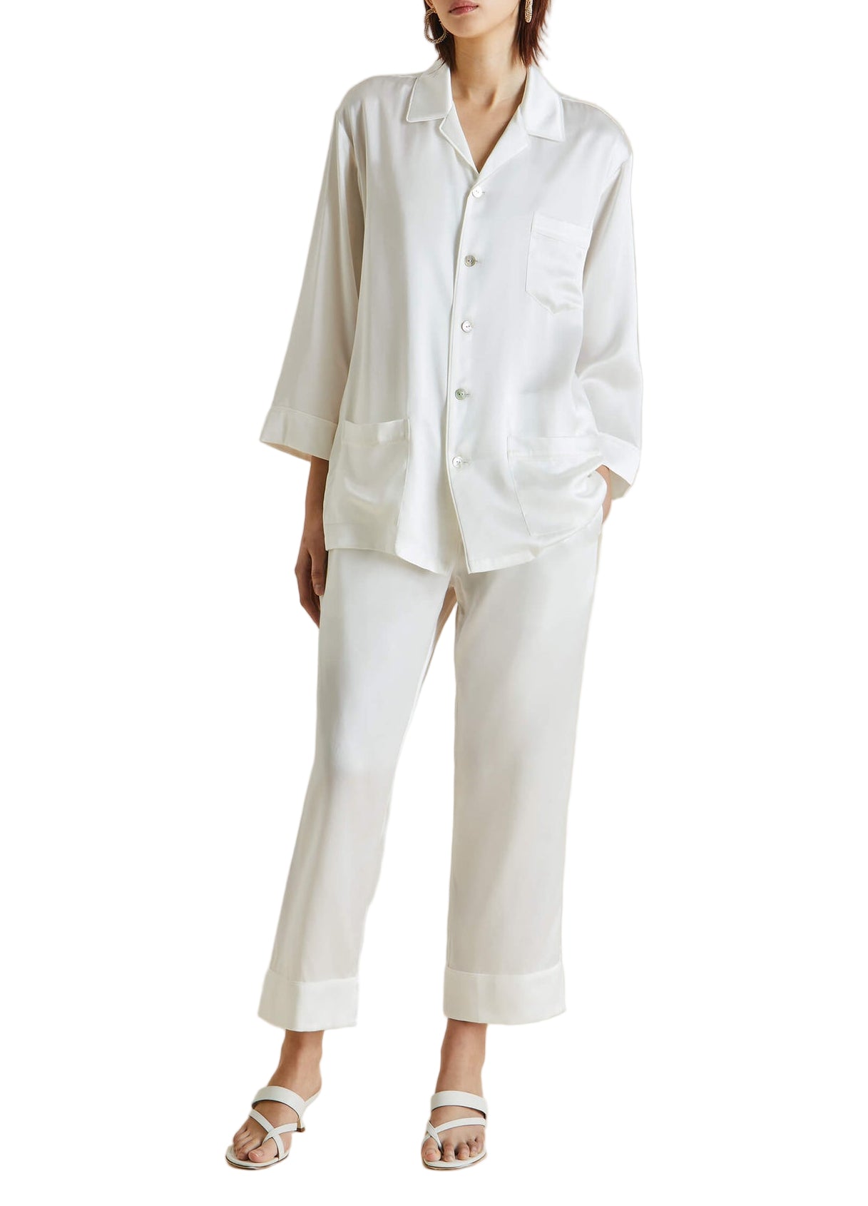 Wearing Olivia von Halle’s Fifi Silk Pajamas with flat sandals, channeling effortless style against a plain background.