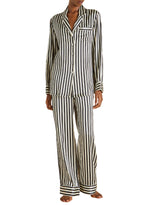A person wearing Olivia von Halle's Lila Silk Pajamas in black and white vertical stripes, featuring long sleeves and pants, stands barefoot.