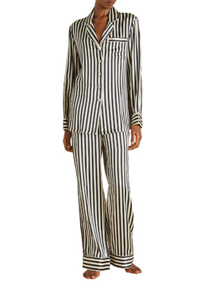 A person wearing Olivia von Halle's Lila Silk Pajamas in black and white vertical stripes, featuring long sleeves and pants, stands barefoot.
