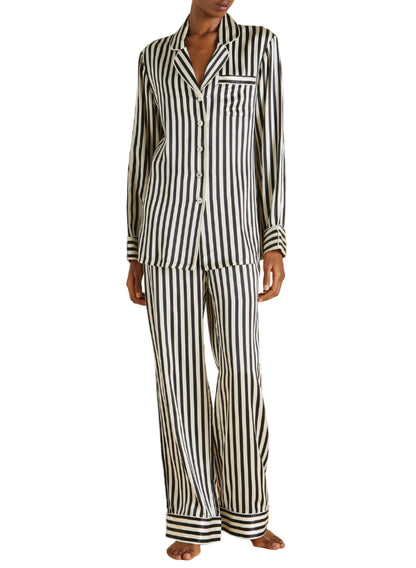 A person wearing Olivia von Halle's Lila Silk Pajamas in black and white vertical stripes, featuring long sleeves and pants, stands barefoot.