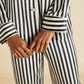 Person wearing Olivia von Halle's Lila Silk Pajamas in classic black and white vertical stripes, showing the torso and hands clasped in front.