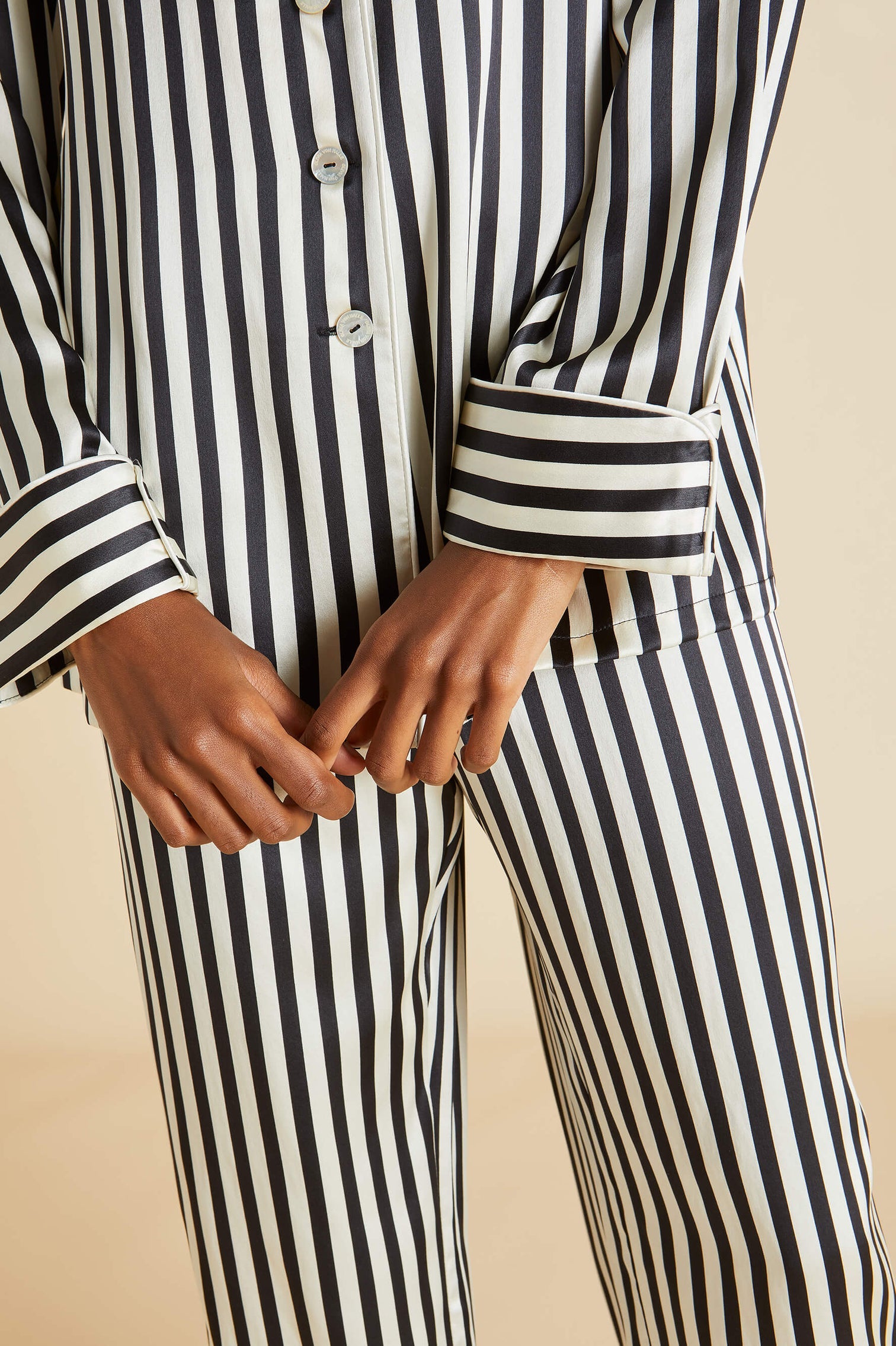 Person wearing Olivia von Halle's Lila Silk Pajamas in classic black and white vertical stripes, showing the torso and hands clasped in front.