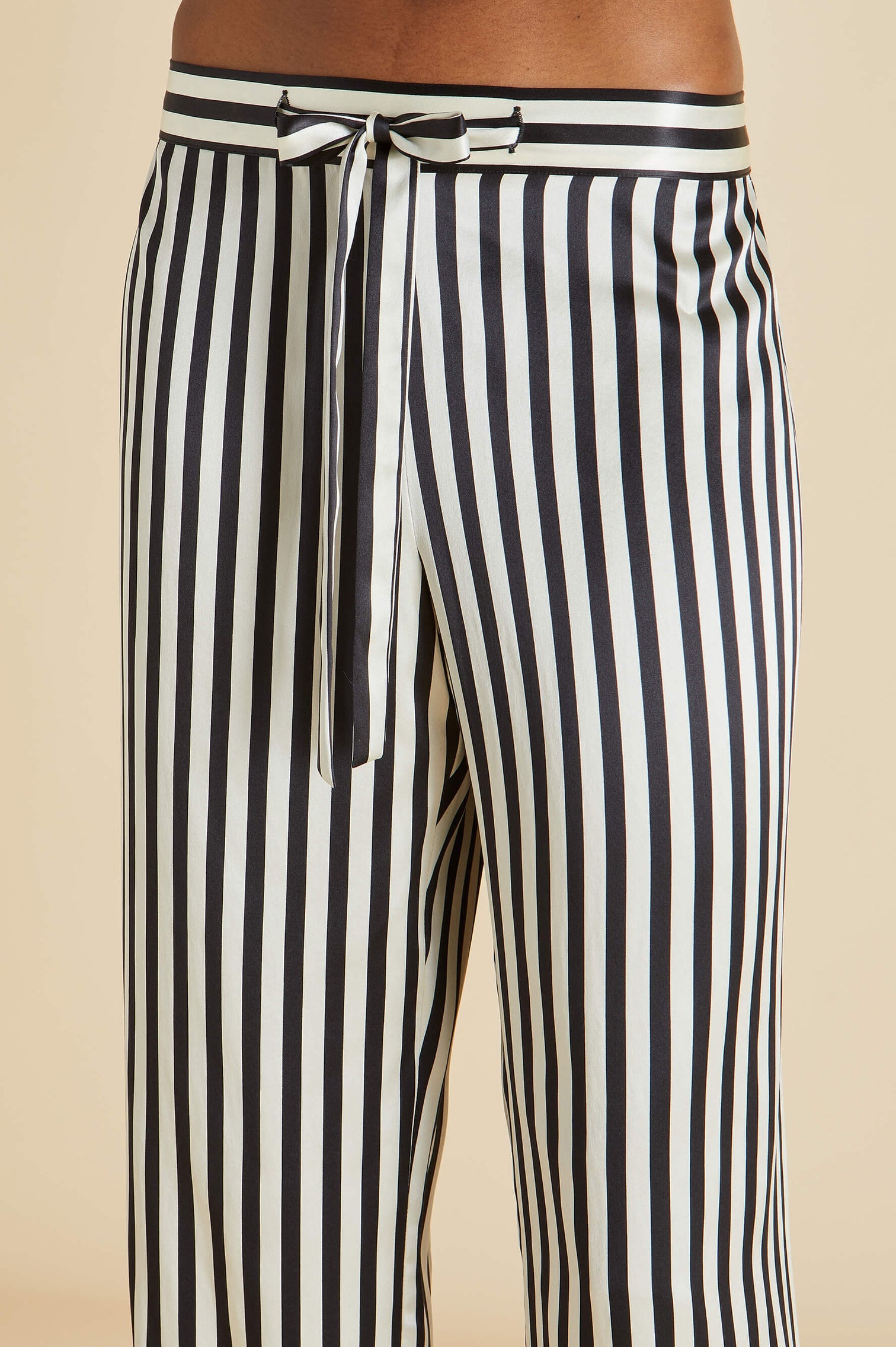 Close-up of Olivia von Halle's Lila Silk Pajamas featuring black and white vertical stripes with a waistband tie—shown from waist to mid-thigh, these elevate your classic pajama look.