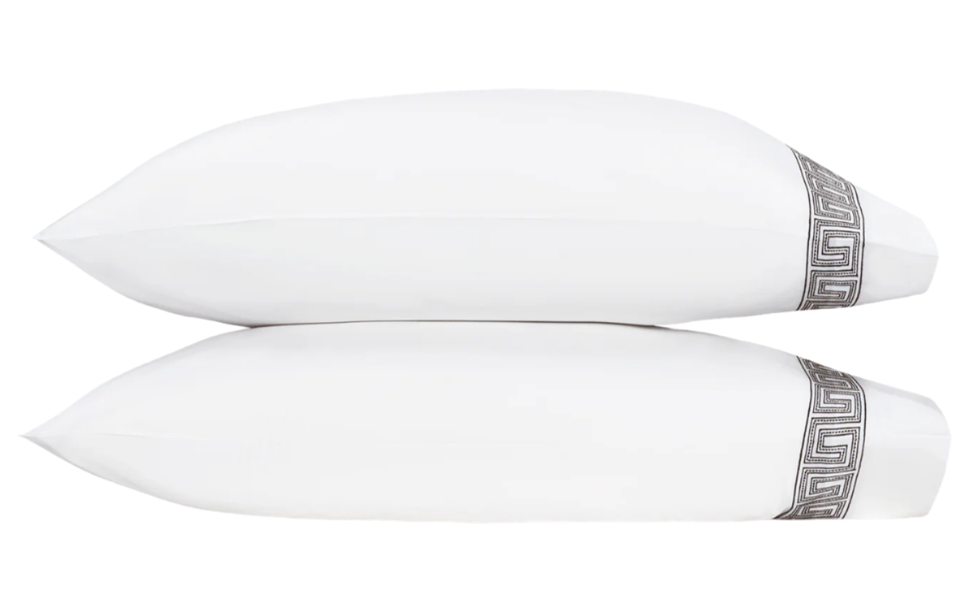 Two rectangular pillows from the Matouk Ophelia Bedding Collection in Mocha, each adorned with a decorative silver Greek key pattern along one edge, are stacked against a plain white background.