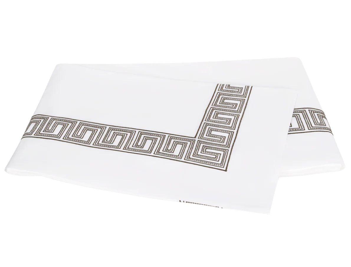 Two folded white sheets from Matouk’s Ophelia Bedding Collection, Mocha, featuring an elegant black and gray Greek key border and crafted from luxurious 520 thread count fabric.