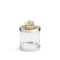 The Michael Aram Orchid Canister is a clear cylindrical glass jar from the Orchid Collection, topped with a silver-colored lid featuring a white flower and gold branch for subtle luxury, purity, and grace.