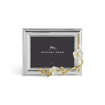 A silver picture frame from the Michael Aram Orchid Frame Collection features gold brass and white enamel orchid accents on one corner, with a black placeholder card labeled "Michael Aram.