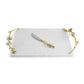The Michael Aram Orchid Serveware Collection features a rectangular white marble serving tray with gold floral handles and a matching cheese knife, reflecting exquisite craftsmanship and timeless elegance.