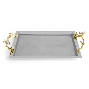 The Michael Aram Orchid Serveware Collection features a rectangular silver tray with gold-toned branch handles and white flower accents, combining elegance and exquisite craftsmanship for timeless gatherings.