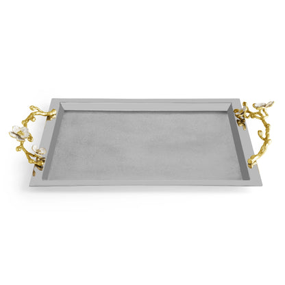 The Michael Aram Orchid Serveware Collection features a rectangular silver tray with gold-toned branch handles and white flower accents, combining elegance and exquisite craftsmanship for timeless gatherings.