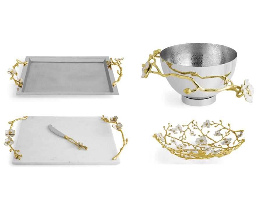 The Michael Aram Orchid Serveware Collection features four pieces—tray, bowl, cheese board with knife, and shallow dish—adorned with gold and white floral branches for elegant, timeless appeal.
