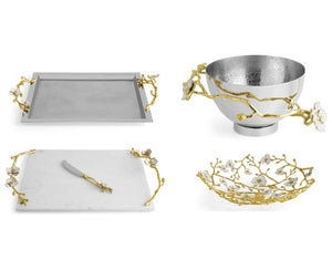 The Michael Aram Orchid Serveware Collection features four pieces—tray, bowl, cheese board with knife, and shallow dish—adorned with gold and white floral branches for elegant, timeless appeal.