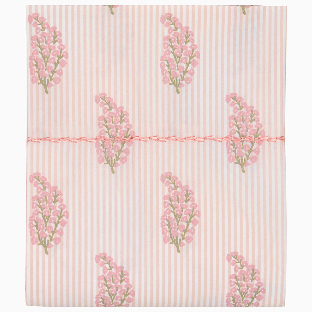The Nirvi Lotus Bedding Collection by John Robshaw features folded fabric with subtle light pink and white stripes, floral block prints in pink and green clusters, and a pink stitched line across the middle.