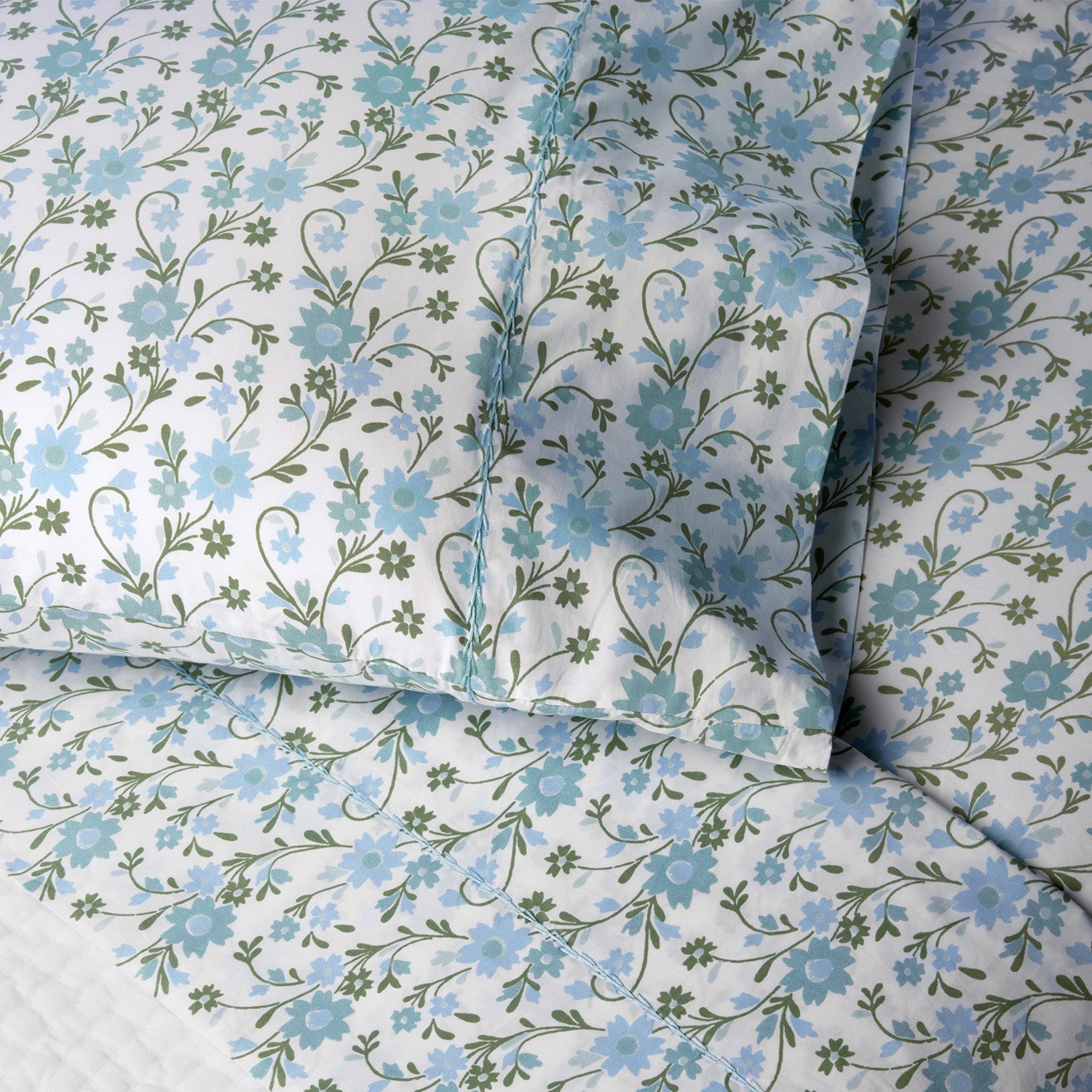 Close-up of a pillow and bed sheet from the John Robshaw Mihana Mist Bedding Collection, featuring a blue and green floral pattern on white 400 thread count organic cotton for botanical harmony in your bedroom.