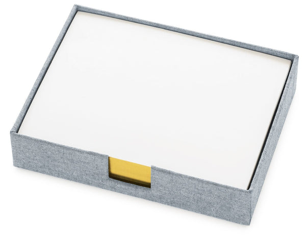 A gray rectangular box with a white lid, accented by a small yellow tab, exudes subtle elegance reminiscent of the Sugar Paper Desk Jotter in Chambray. This design perfectly blends functionality and style, capturing sophisticated charm.