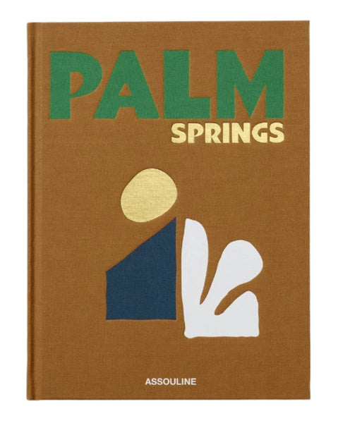 The Assouline book cover, titled "Palm Springs," showcases abstract shapes in green, blue, yellow, and white set against a brown background, capturing the essence of a mid-century modern desert oasis.