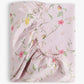 The Gooselings Dreaming of Paradise Crib Sheet is a folded pink cotton sateen sheet with elastic edges, adorned with green vines and yellow and pink flowers. OEKO-TEX certified for safety and comfort.