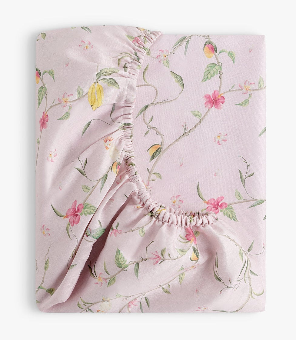 The Gooselings Dreaming of Paradise Crib Sheet is a folded pink cotton sateen sheet with elastic edges, adorned with green vines and yellow and pink flowers. OEKO-TEX certified for safety and comfort.