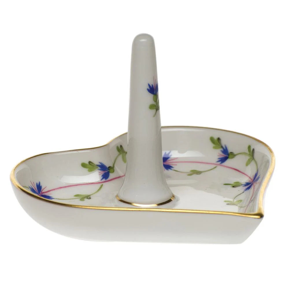 The Herend Ring Holder is a heart-shaped, hand-painted porcelain piece featuring a central upright post, delicate blue flower accents, and elegant gold trim.
