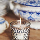 A Baobab Collection Gentlemen Body Wellness candle with a masculine scent rests on a wooden surface beside blue and white ceramic dishes.