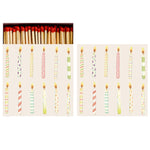 A Hester & Cook Box of 60 Matches with red tips rests above two rows of lit, striped and patterned birthday candles on a light background.