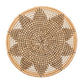 A round, woven seagrass basket tray with a tan, brown, and white starburst pattern pairs perfectly with Kim Seybert’s Majorelle Placemat.