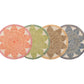 Four round Kim Seybert Majorelle Placemats, in orange, green, beige, and blue with geometric star designs and white floral-inspired accents, are displayed side by side.