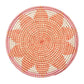 The Majorelle Placemat by Kim Seybert, crafted from natural seagrass, displays an orange, white, and pink geometric pattern with subtle floral motifs. Photographed from above on a white background.