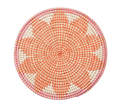 The Majorelle Placemat by Kim Seybert, crafted from natural seagrass, displays an orange, white, and pink geometric pattern with subtle floral motifs. Photographed from above on a white background.