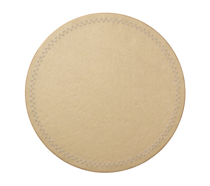 The Starry Night Placemat Collection by Kim Seybert features a round, beige leather coaster with metallic trim and visible stitched edges. Photographed on a white background, it offers effortless cleaning while adding style to your table.