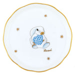 The Herend Bunny Coaster is handcrafted in Hungary from fine porcelain and features a cartoon rabbit holding a blue patterned egg, gold stars, and the Herend brand name.