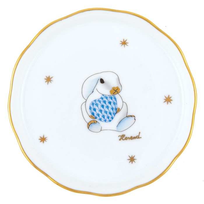 The Herend Bunny Coaster is handcrafted in Hungary from fine porcelain and features a cartoon rabbit holding a blue patterned egg, gold stars, and the Herend brand name.