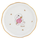 Herend Bunny Coaster: White porcelain with a gold rim, featuring a bunny holding a pink patterned egg, gold stars, and the word "Herend." Handcrafted in Hungary.