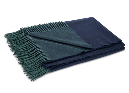 The Matouk Paley Cashmere Throw, a folded reversible design in navy blue and dark green with green fringed edges, is shown on a plain light background.