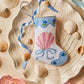 The Let's Shellebrate Needle Point Stocking by Bauble Stockings features a seashell and ribbon design—displayed with shells and ribbons, it adds a Palm Beach Lately touch to your coastal holiday decor.