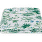 The Palmyra Bedding Collection in Emerald by Matouk features a neatly folded white bedsheet adorned with green palm fronds and a floral print on a plain background.