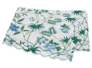 The Matouk Palmyra Bedding Collection, Emerald, features a folded tablecloth with green and blue palm fronds and leafy patterns on a white background, finished with a scalloped edge.